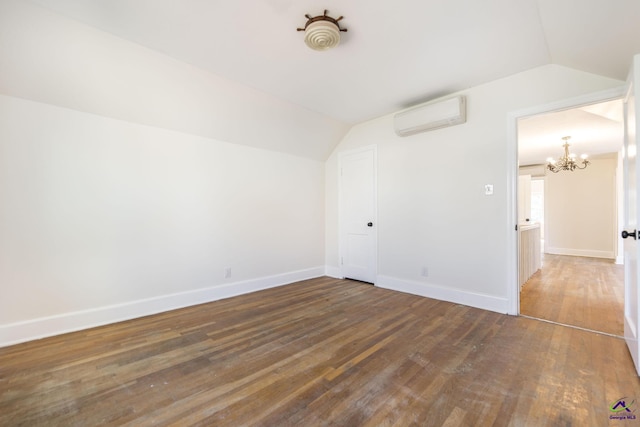 spare room featuring a chandelier, lofted ceiling, a wall unit AC, and hardwood / wood-style floors