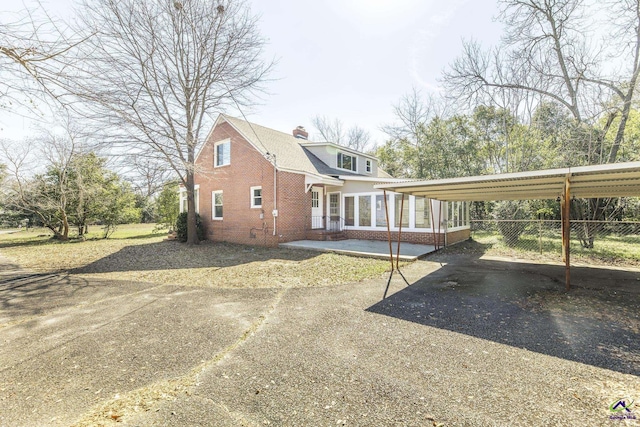 exterior space featuring brick siding, fence, aphalt driveway, a sunroom, and a carport