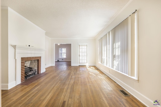 unfurnished living room with visible vents, a textured ceiling, wood finished floors, and ornamental molding