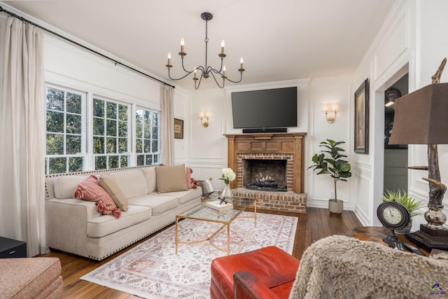 living room with a brick fireplace, a chandelier, ornamental molding, hardwood / wood-style floors, and a decorative wall