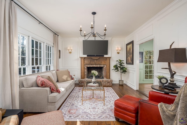 living room with dark wood finished floors, a brick fireplace, crown molding, a decorative wall, and a chandelier