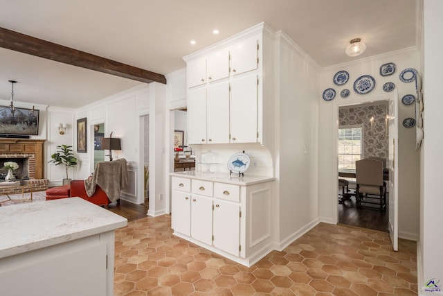 kitchen with beam ceiling, white cabinets, crown molding, light stone countertops, and a brick fireplace