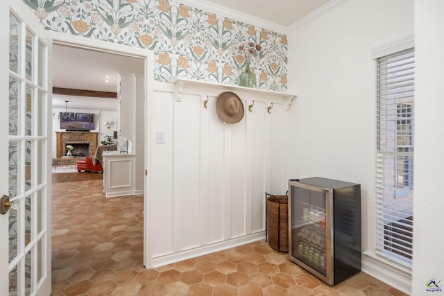 mudroom featuring beverage cooler, a brick fireplace, wallpapered walls, and crown molding