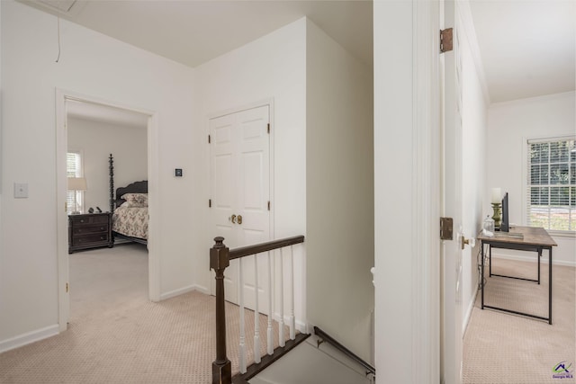 corridor with an upstairs landing, light colored carpet, attic access, and baseboards