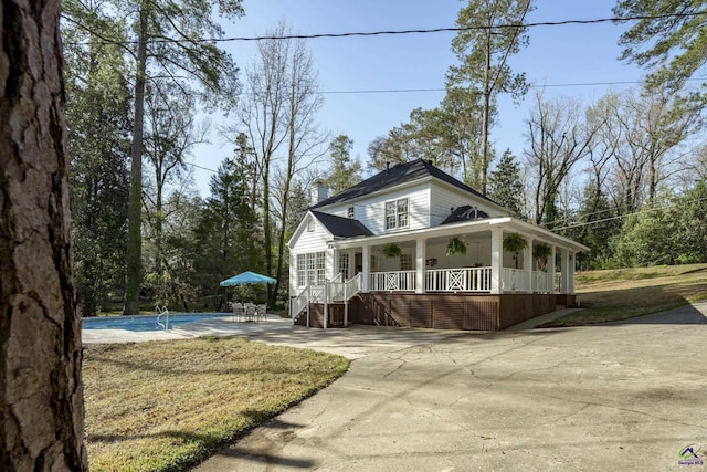 view of front facade featuring an outdoor pool, covered porch, driveway, and a chimney