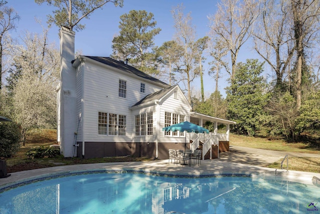 rear view of property with stairway, a wooden deck, a chimney, a patio area, and an outdoor pool