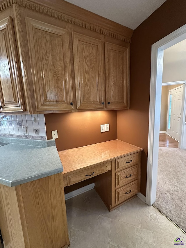 unfurnished office with baseboards, light colored carpet, and built in desk