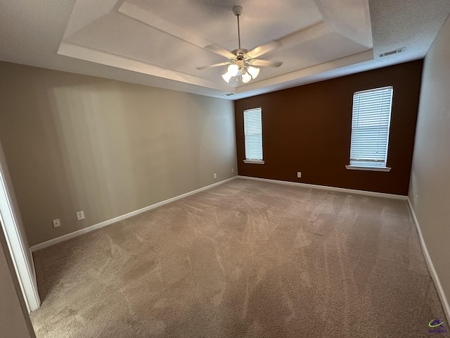 empty room with visible vents, baseboards, carpet floors, a raised ceiling, and a ceiling fan