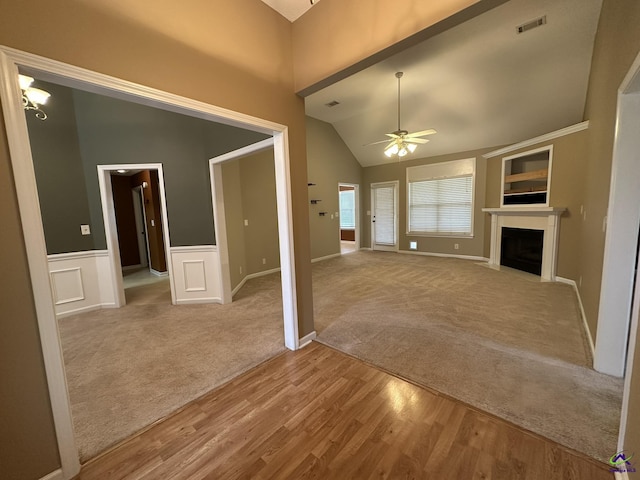 unfurnished living room featuring a ceiling fan, visible vents, carpet floors, a fireplace with flush hearth, and wainscoting