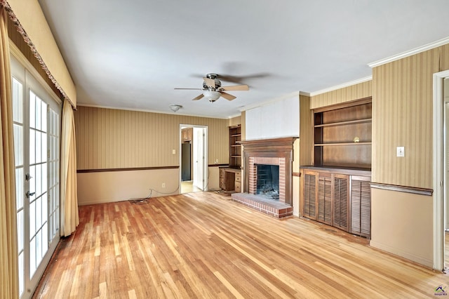 unfurnished living room featuring ornamental molding, a fireplace, a ceiling fan, and light wood finished floors