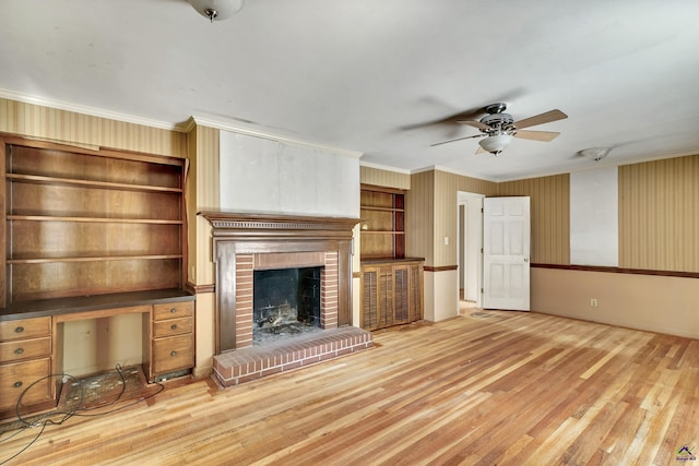 unfurnished living room with a brick fireplace, crown molding, ceiling fan, and wood finished floors