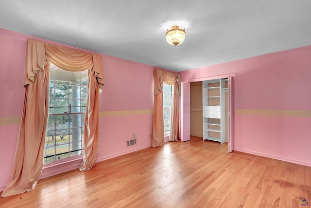 unfurnished room featuring a wealth of natural light, visible vents, light wood-style flooring, and baseboards