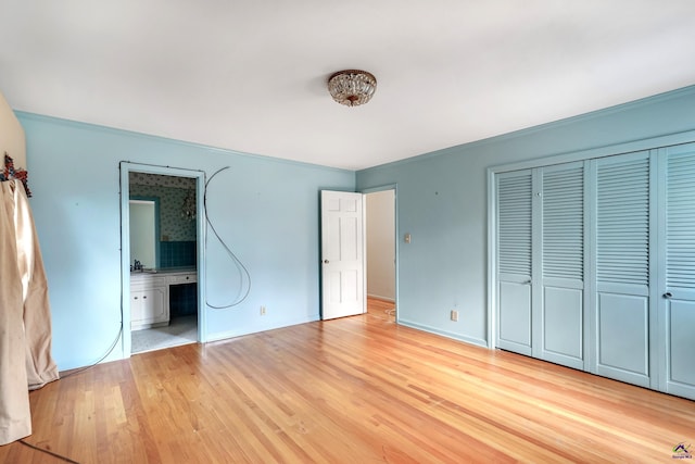 unfurnished bedroom with a closet, light wood-style flooring, ensuite bathroom, and baseboards