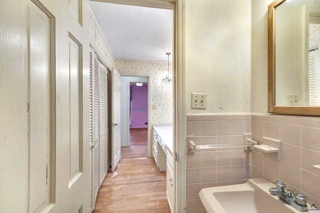 bathroom featuring wood finished floors, wallpapered walls, ornamental molding, a sink, and wainscoting