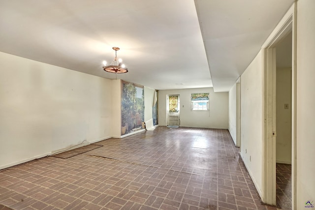 empty room featuring brick floor, baseboards, and an inviting chandelier