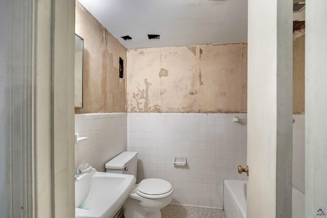 bathroom with toilet, wainscoting, tile patterned floors, tile walls, and a sink