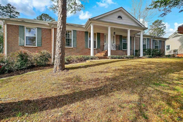 neoclassical home featuring brick siding, covered porch, and a front lawn