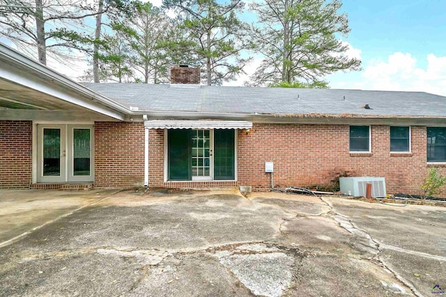 rear view of house with brick siding, central AC unit, french doors, a chimney, and a patio area