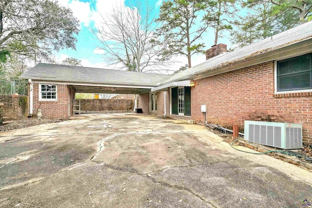 exterior space featuring brick siding, concrete driveway, central AC unit, a chimney, and a carport