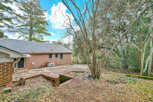 rear view of property with brick siding, a chimney, central AC, and a patio