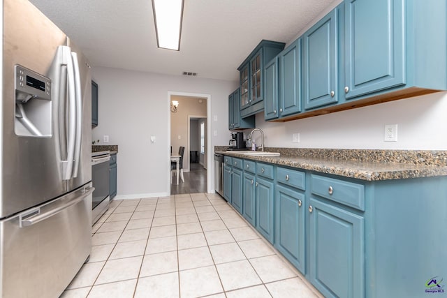 kitchen with dark countertops, visible vents, blue cabinetry, appliances with stainless steel finishes, and a sink