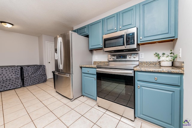 kitchen with blue cabinetry, a textured ceiling, appliances with stainless steel finishes, and light tile patterned floors