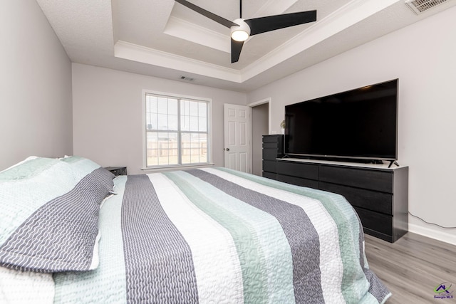 bedroom with light wood-type flooring, visible vents, a raised ceiling, and ornamental molding