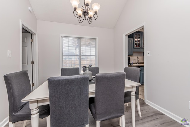 dining room featuring vaulted ceiling, baseboards, light wood finished floors, and a chandelier