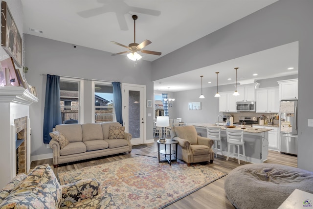 living room featuring light wood finished floors, visible vents, lofted ceiling, ceiling fan with notable chandelier, and a fireplace