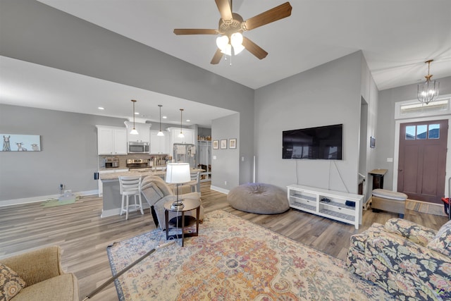 living room with light wood finished floors, recessed lighting, ceiling fan with notable chandelier, and baseboards