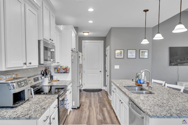 kitchen featuring light wood-type flooring, an island with sink, a sink, appliances with stainless steel finishes, and white cabinets