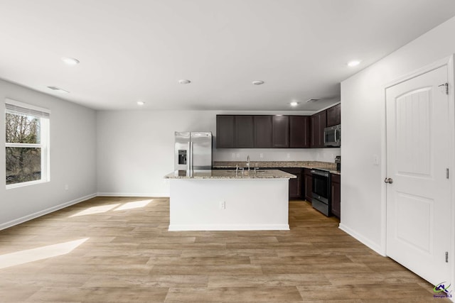 kitchen featuring an island with sink, light stone counters, light wood-style flooring, appliances with stainless steel finishes, and a sink