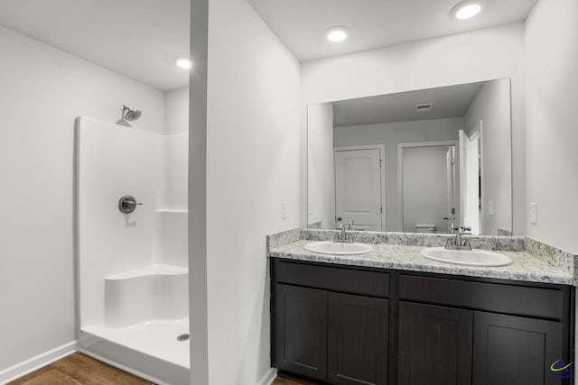 full bath featuring double vanity, a shower, and a sink