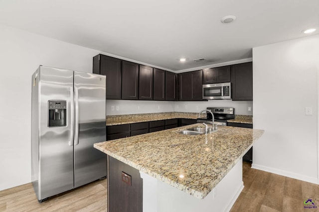 kitchen with visible vents, a sink, stainless steel appliances, light wood finished floors, and light stone countertops