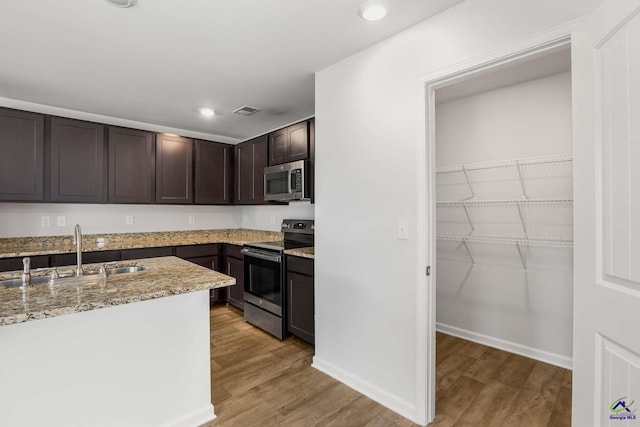 kitchen with visible vents, a sink, stainless steel appliances, dark brown cabinetry, and light wood finished floors