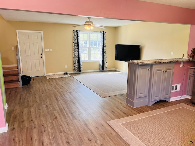 unfurnished living room with stairway, baseboards, visible vents, light wood finished floors, and ceiling fan