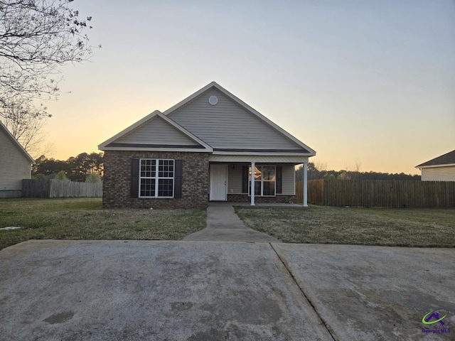 view of front of house featuring brick siding, a lawn, a porch, and fence