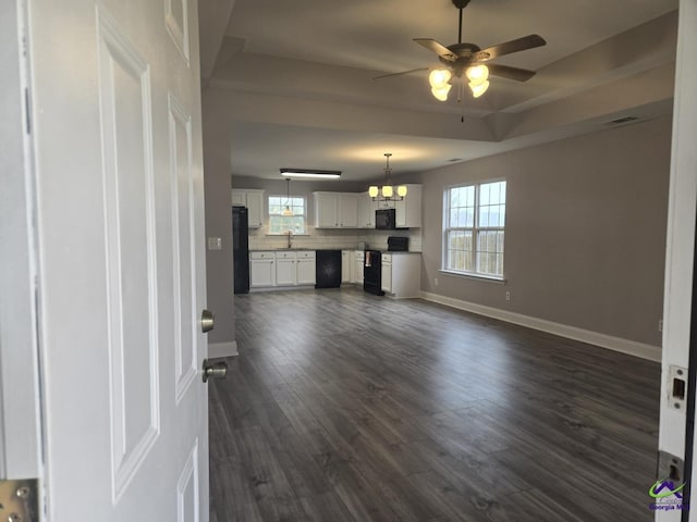 unfurnished living room with baseboards, a raised ceiling, dark wood finished floors, and ceiling fan with notable chandelier