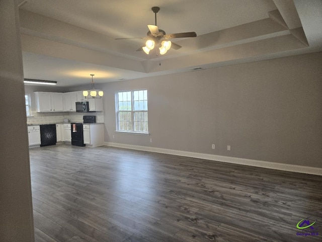 unfurnished living room featuring ceiling fan with notable chandelier, baseboards, a raised ceiling, and dark wood-type flooring