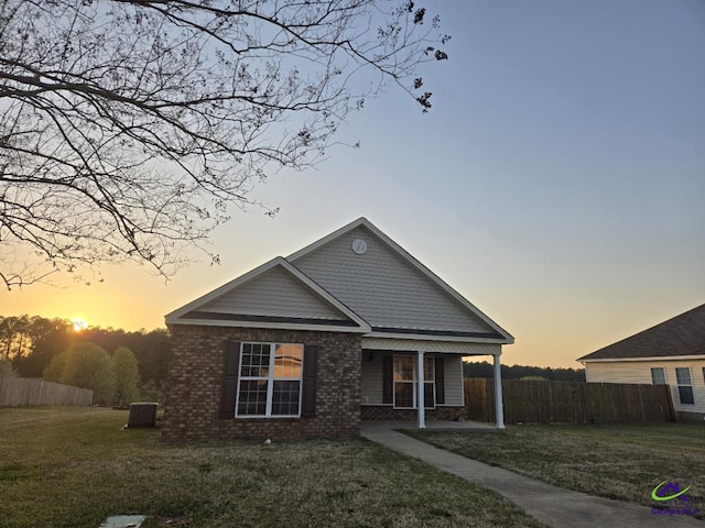 view of front of house featuring central air condition unit, covered porch, a front lawn, and fence