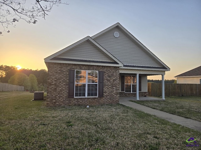 back of house with brick siding, central AC unit, a lawn, and fence