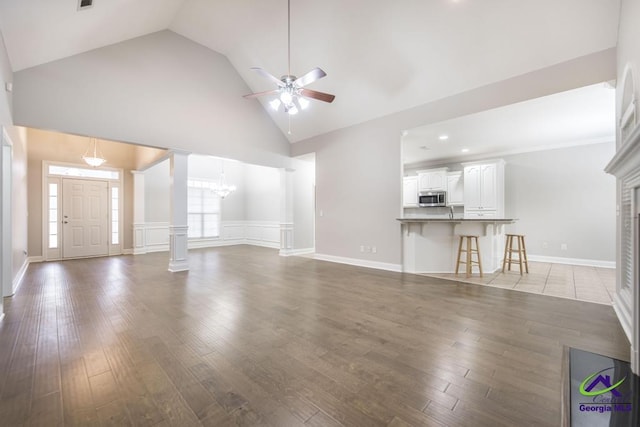 unfurnished living room with ceiling fan with notable chandelier, a fireplace, high vaulted ceiling, and wood finished floors