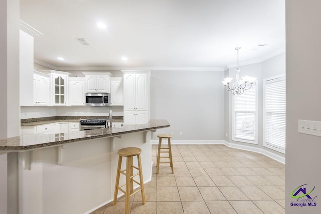 kitchen with a kitchen bar, ornamental molding, dark stone countertops, appliances with stainless steel finishes, and white cabinets