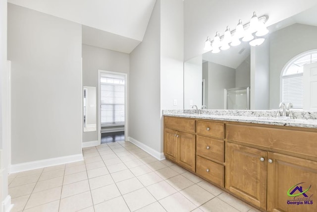 full bath featuring tile patterned floors, a shower with shower door, double vanity, baseboards, and vaulted ceiling