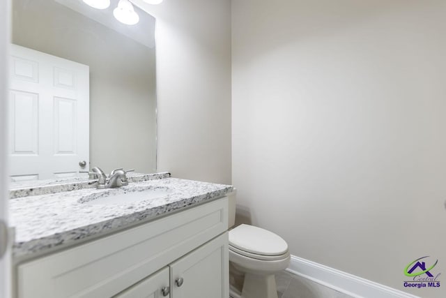 half bathroom with tile patterned floors, baseboards, toilet, and vanity