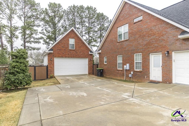 view of side of property featuring brick siding, roof with shingles, a garage, and fence