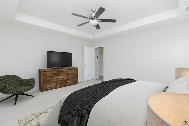 bedroom with visible vents, baseboards, a tray ceiling, light carpet, and a ceiling fan