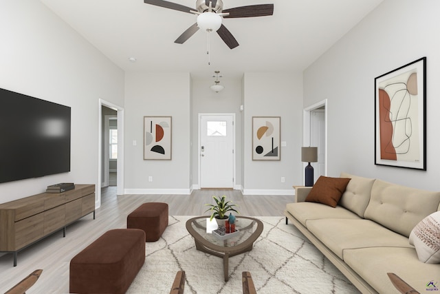 living room featuring light wood finished floors, baseboards, and ceiling fan