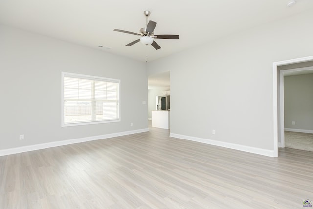 spare room with a ceiling fan, visible vents, light wood finished floors, and baseboards