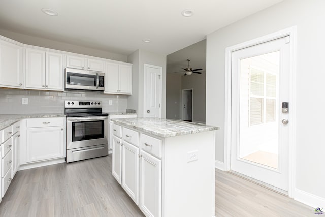 kitchen with light wood finished floors, stainless steel appliances, decorative backsplash, white cabinetry, and a center island